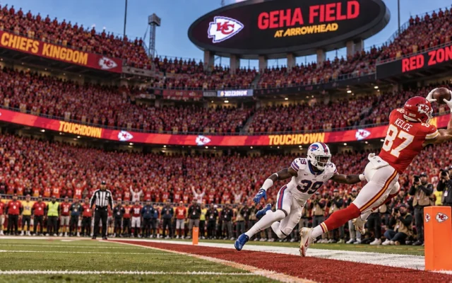 Recebedor de uniforme vermelho dos Chiefs mergulha para pegar um passe na red zone, com a arquibancada lotada ao fundo