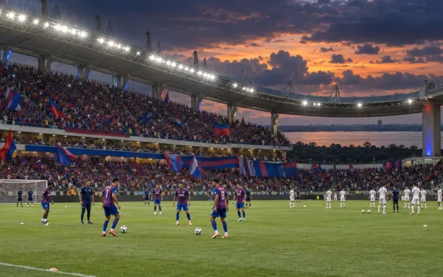 Mangueirão lotado ao entardecer, com bandeiras azuis e vermelhas e jogadores aquecendo sob refletores, incluindo o Santos inteiramente de branco