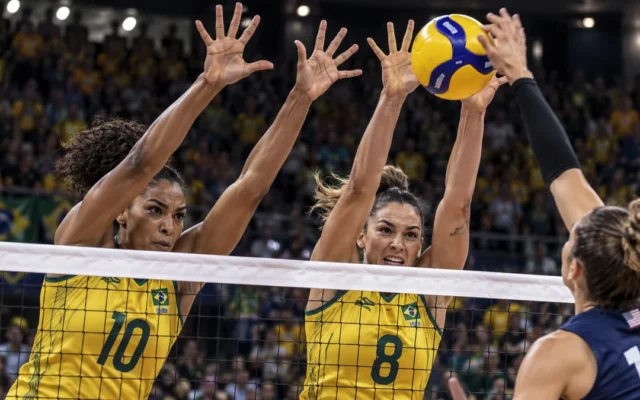 Jogadoras de amarelo formam bloqueio duplo na rede para defender um ataque